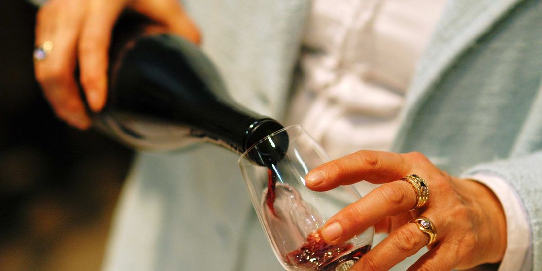 Red wine being poured from a bottle into a tasting glass, held in two hands