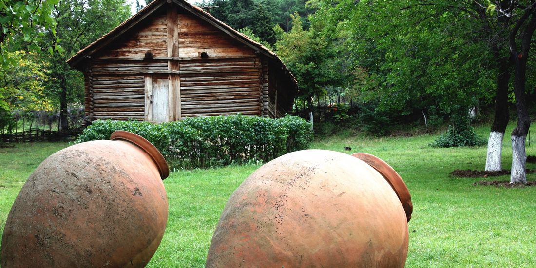 Two large clay qvevri lying on the grass outside a wooden house in Georgia